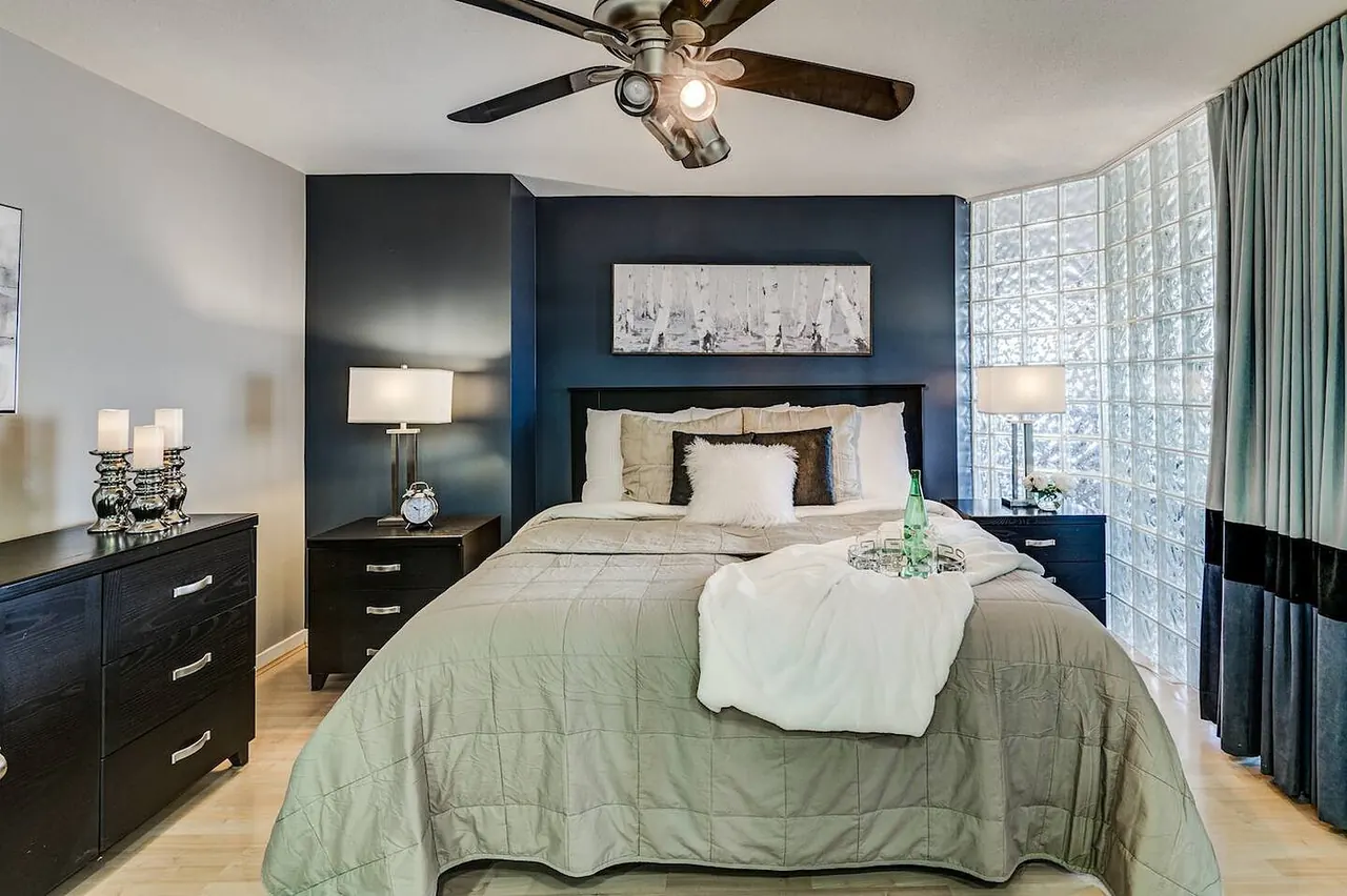 Primary bedroom with a ceiling fan and a glass-block wall